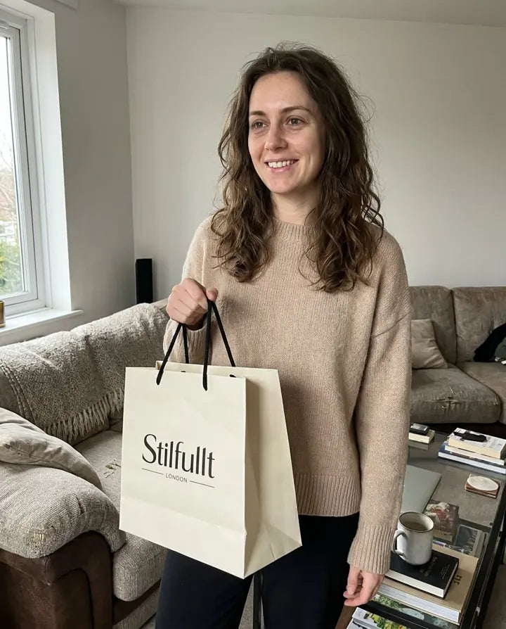 Woman in beige jumper holding a Stilfullt London bag at home